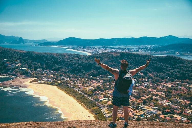 man standing with outspread arms on mountain looking at sea