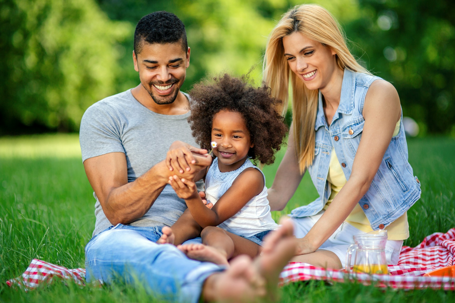 parents and a young child sitting on a picnic blanket in a park