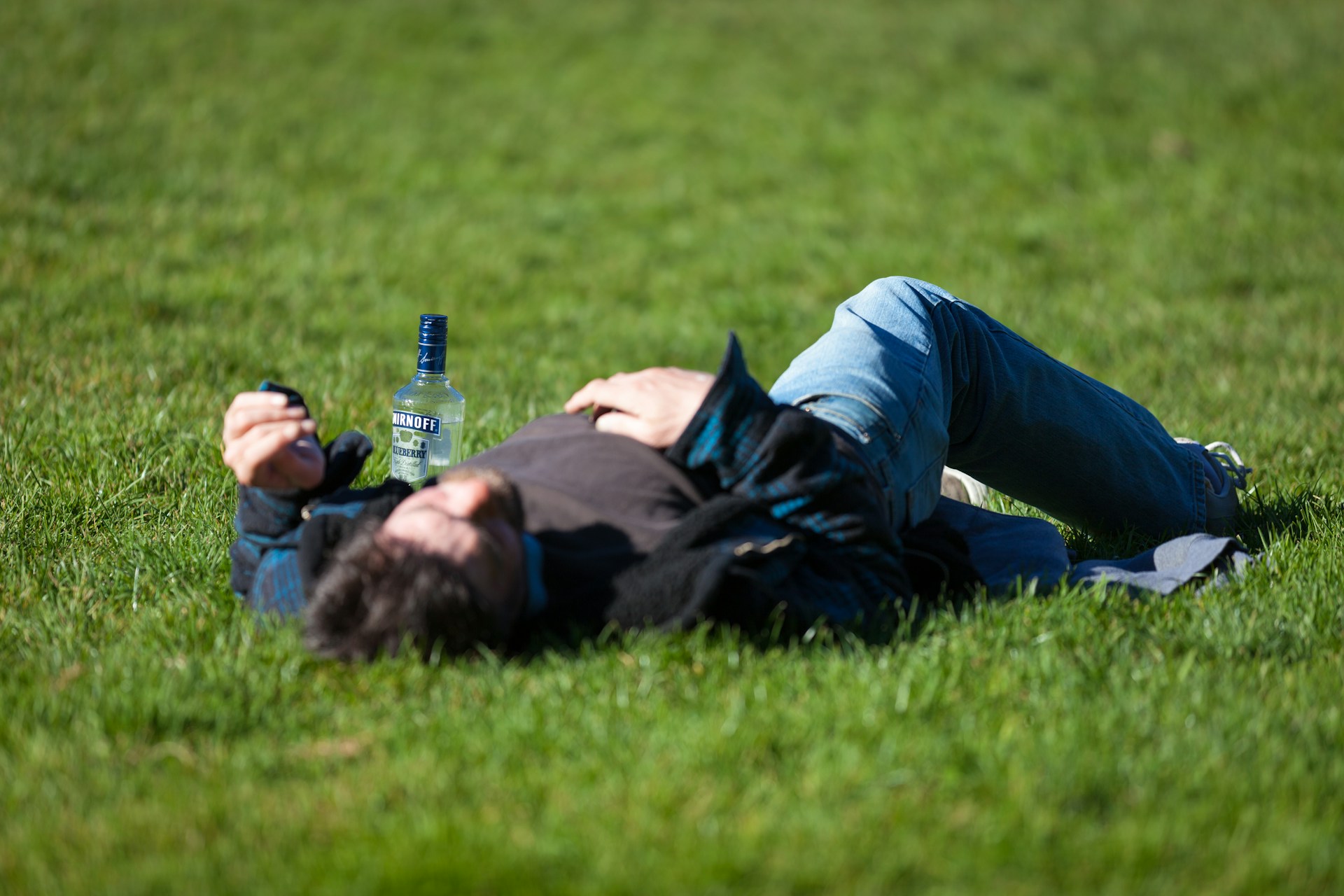 drunk man lying on grass next to an empty bottle