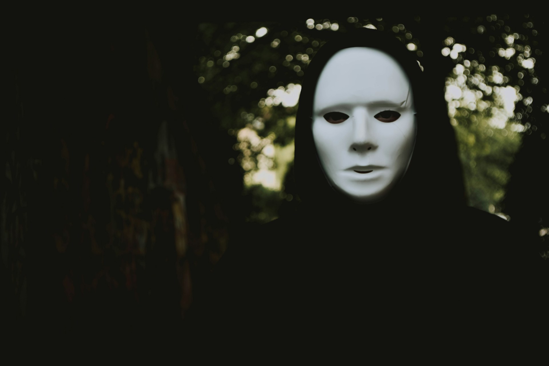 Hooded person wearing a white expressionless mask