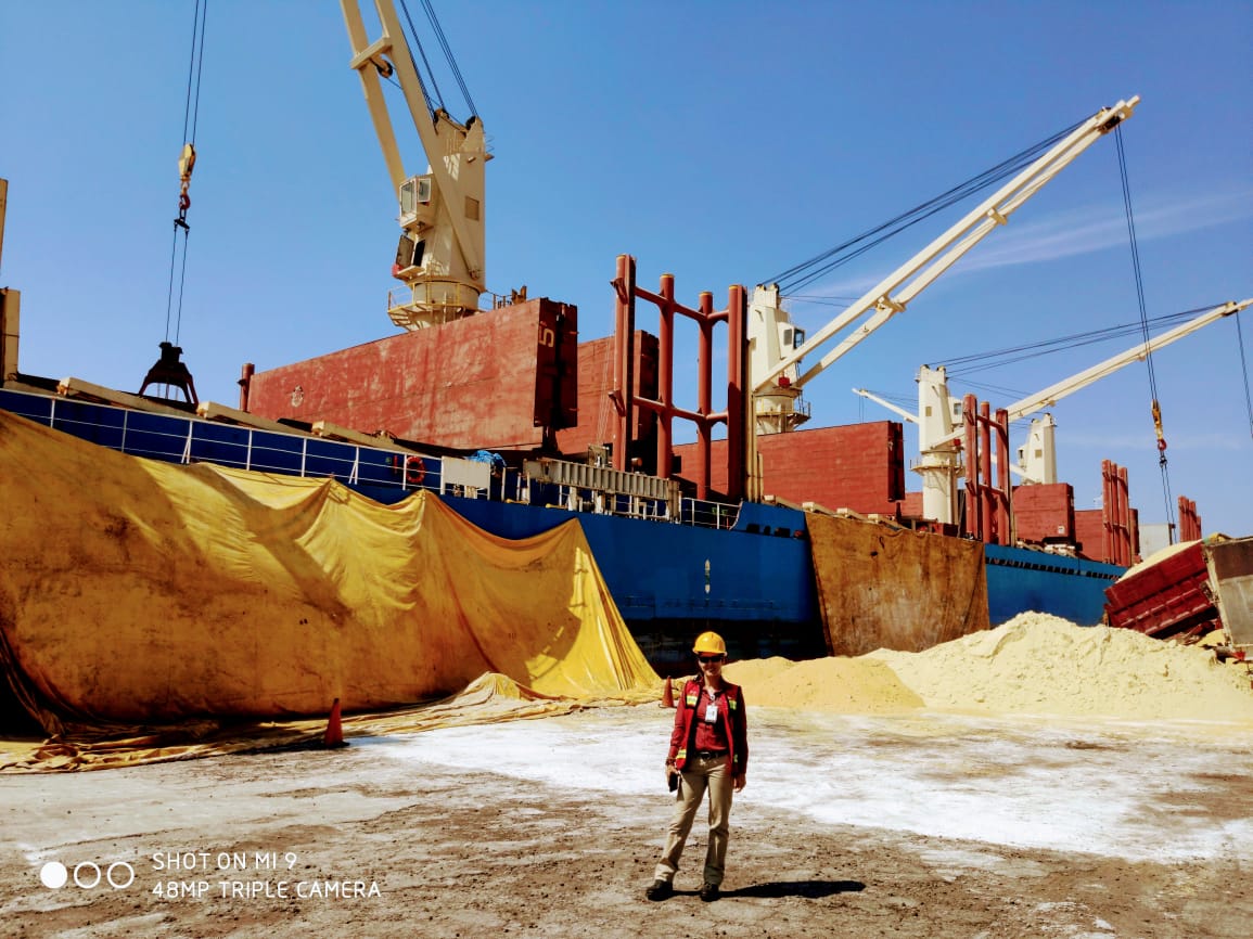 Person working in a maritime job standing near a bulk carrier docked and loading or unloading a cargo of sand