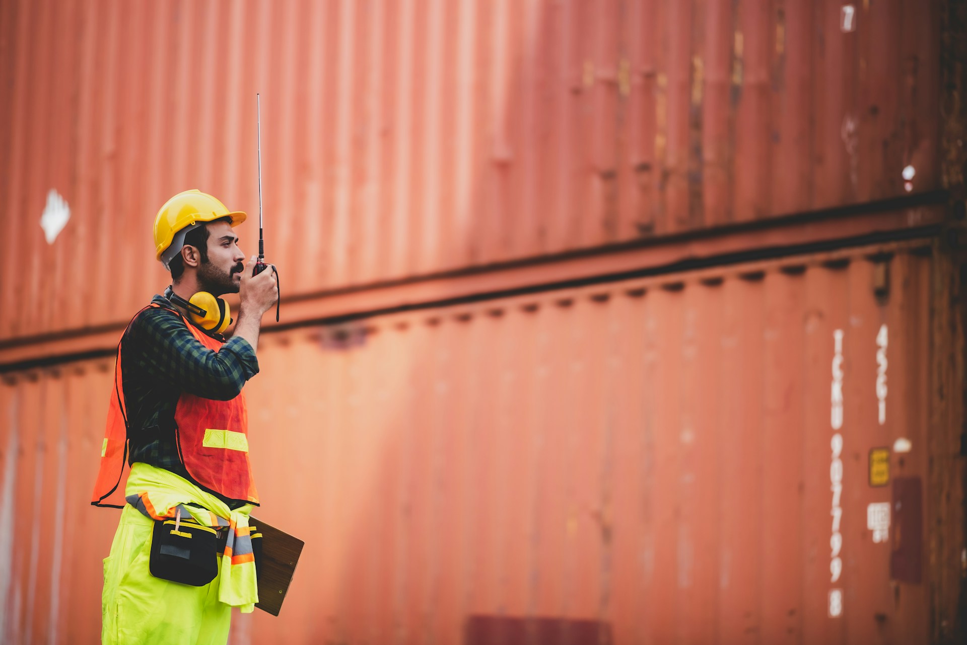 A man in hi vis safety gear talking into a radio while looking at a shipping container