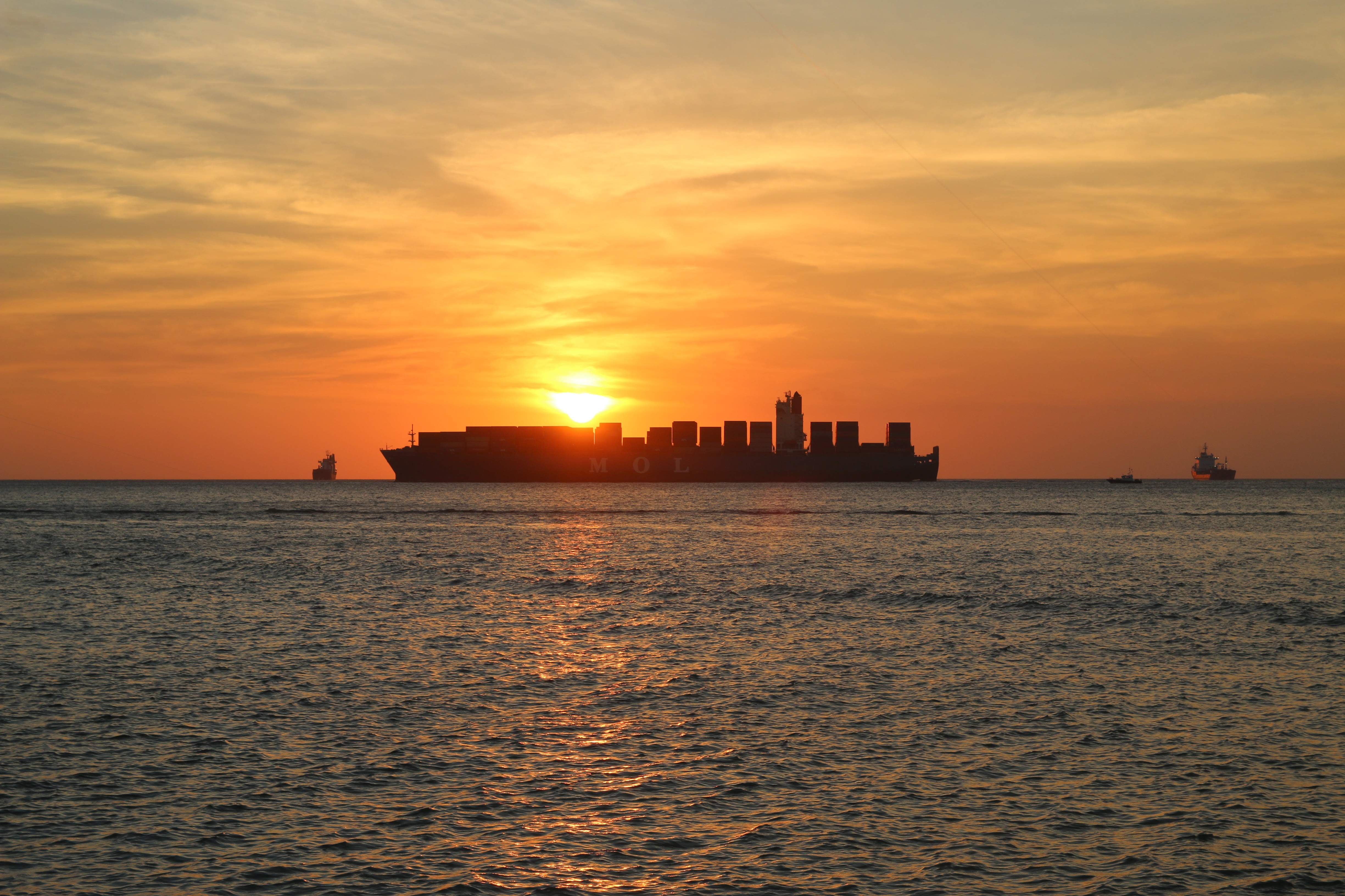 The silhouette of a container ship on the horizon at sunset