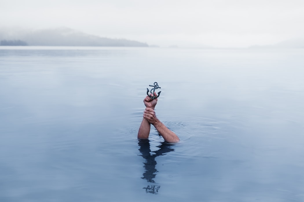 a hand holding a small anchor out of a body of water