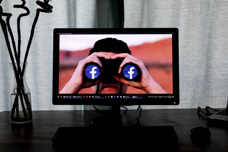 a man on a computer monitor looking through binoculars with the Facebook logo in their lenses