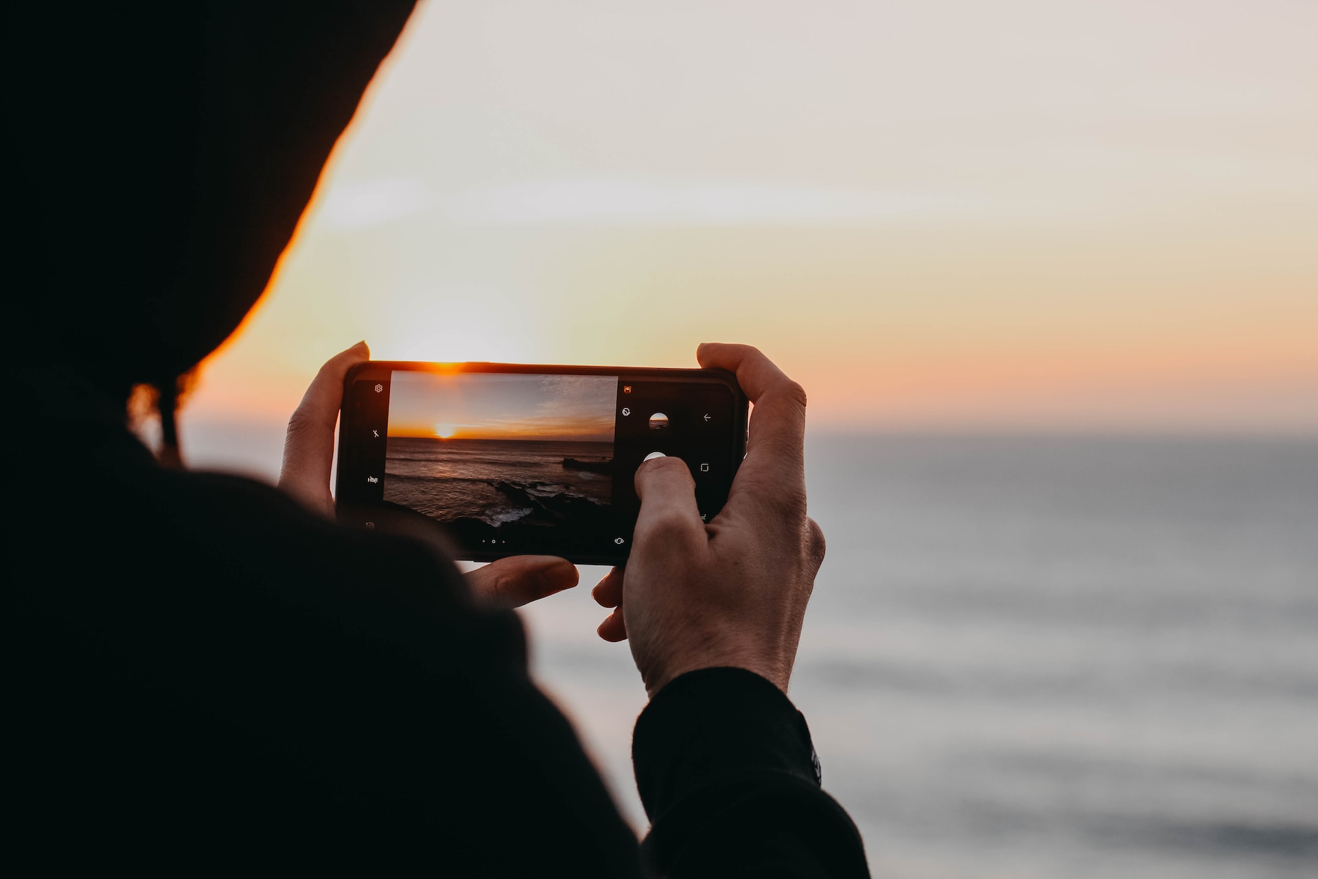 person taking a photo with their phone of a sunset at sea