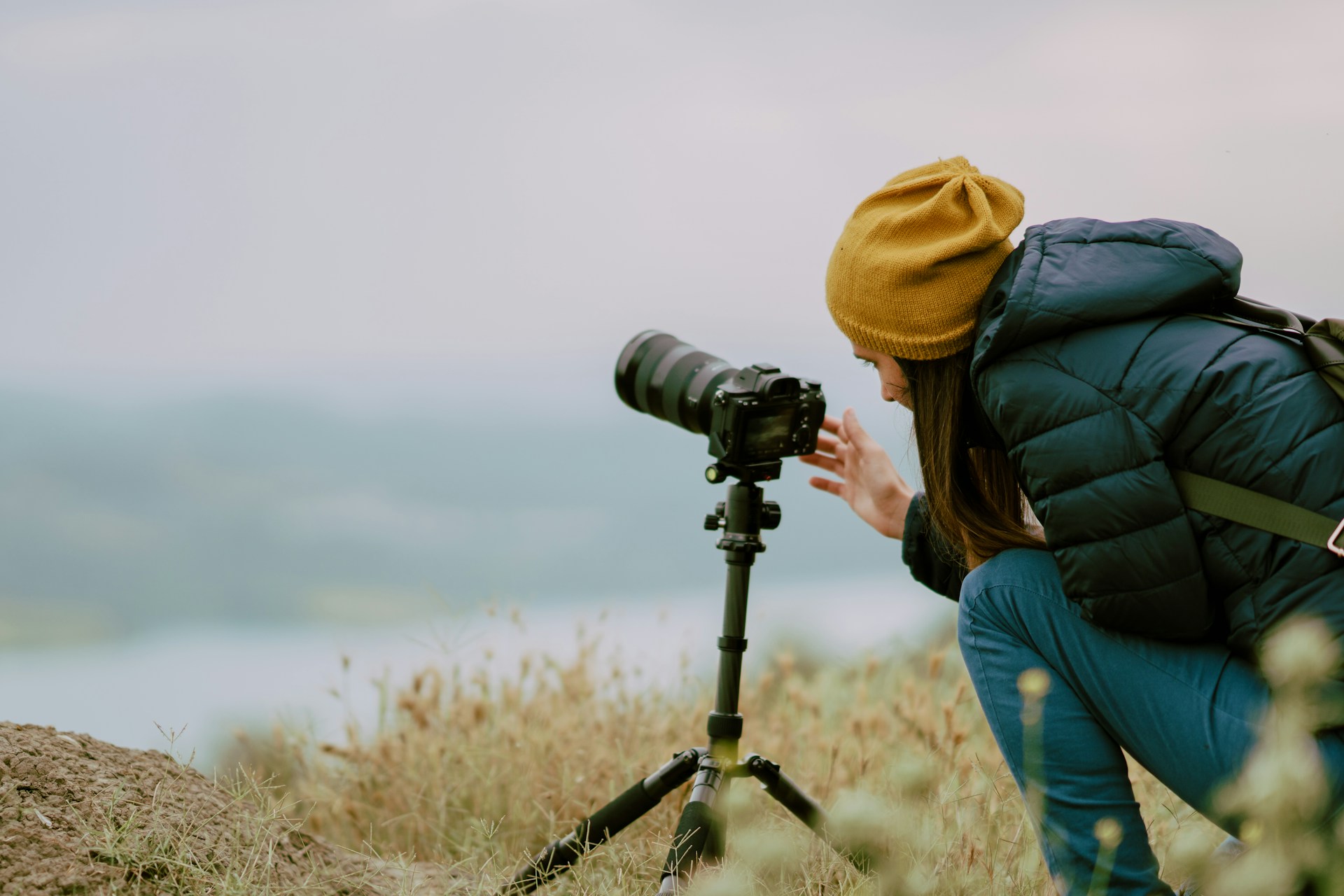 a woman on a cliff taking photographs of a lake