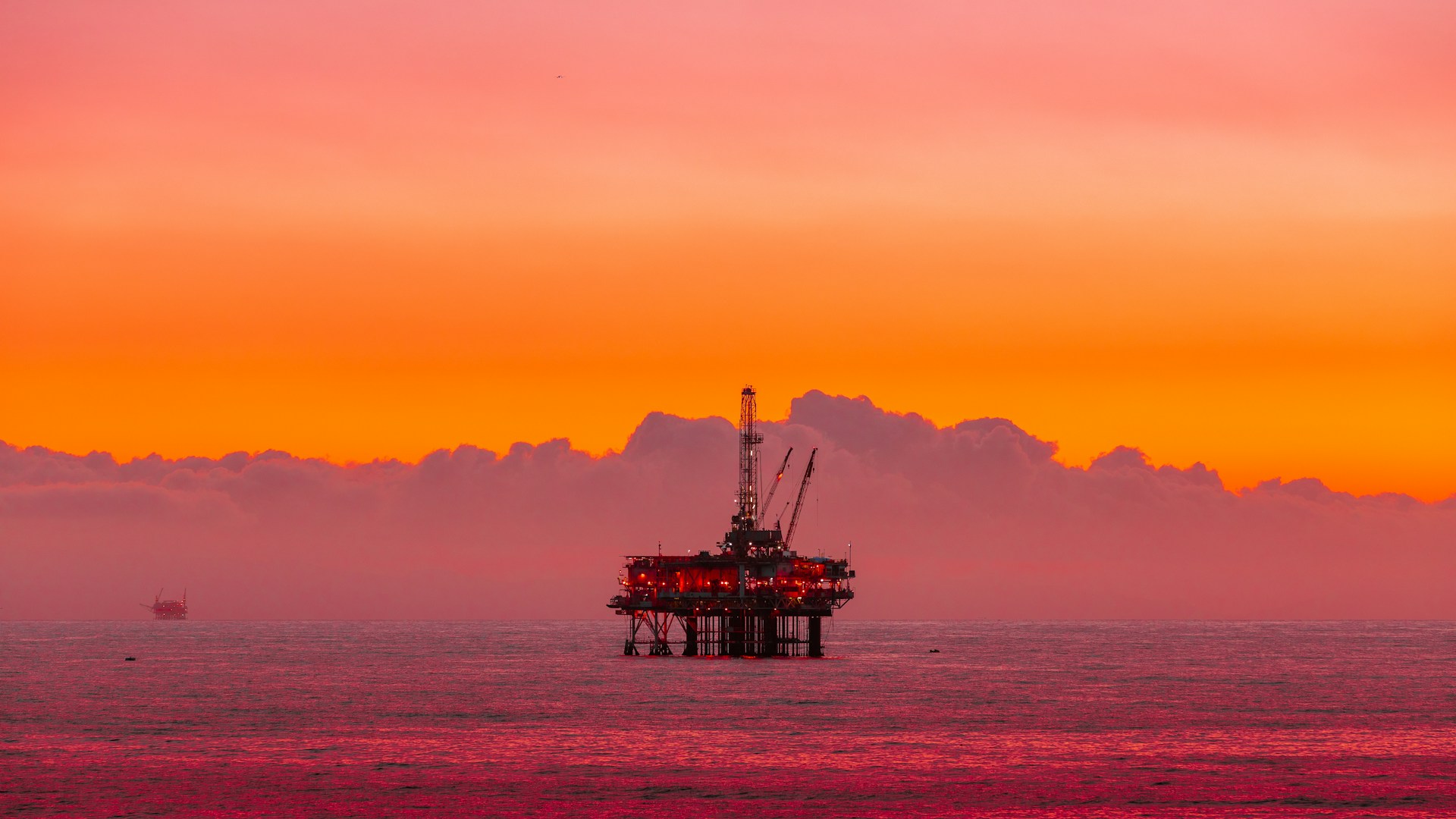An offshore oil rig under a pink and orange sunset
