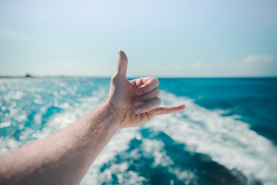 a hand making a hang loose sign off the stern of a small boat