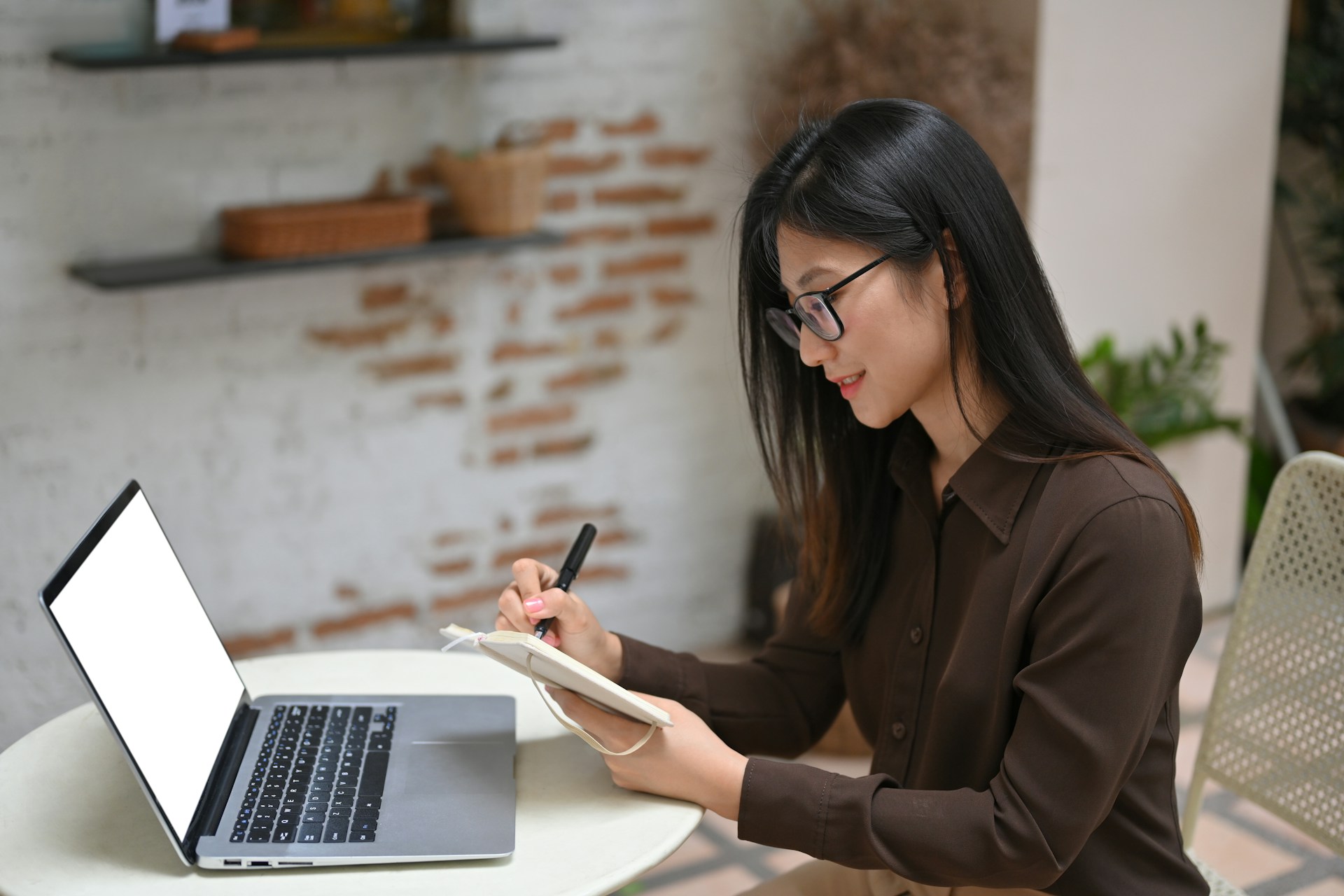 a woman using a laptop while also taking notes