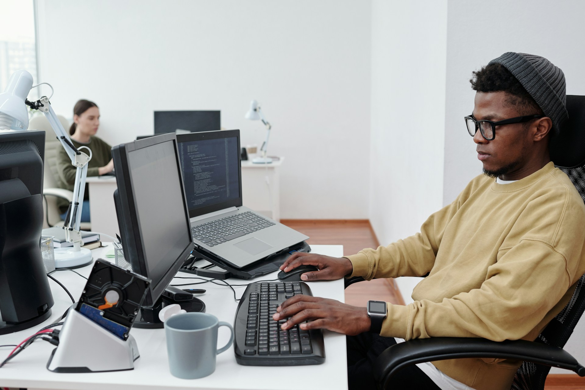 A techie looking guy with a laptop and monitor on his desk