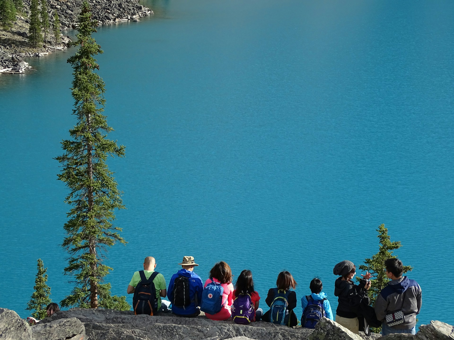 tourists with backpacks sitting on a cliff overlooking blue water 