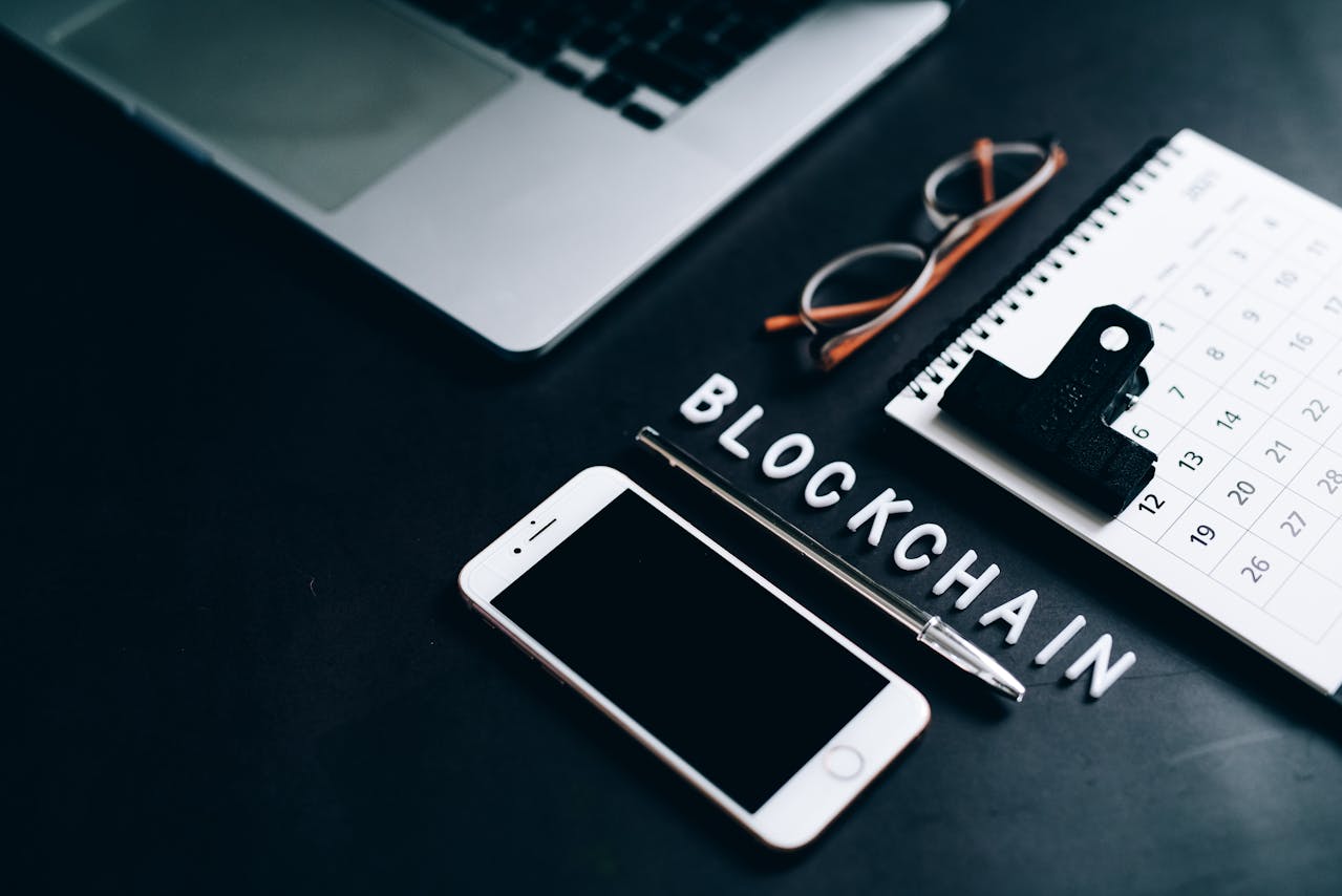 a desk with laptop, phone, calendar and letters spelling out 'blockchain' 