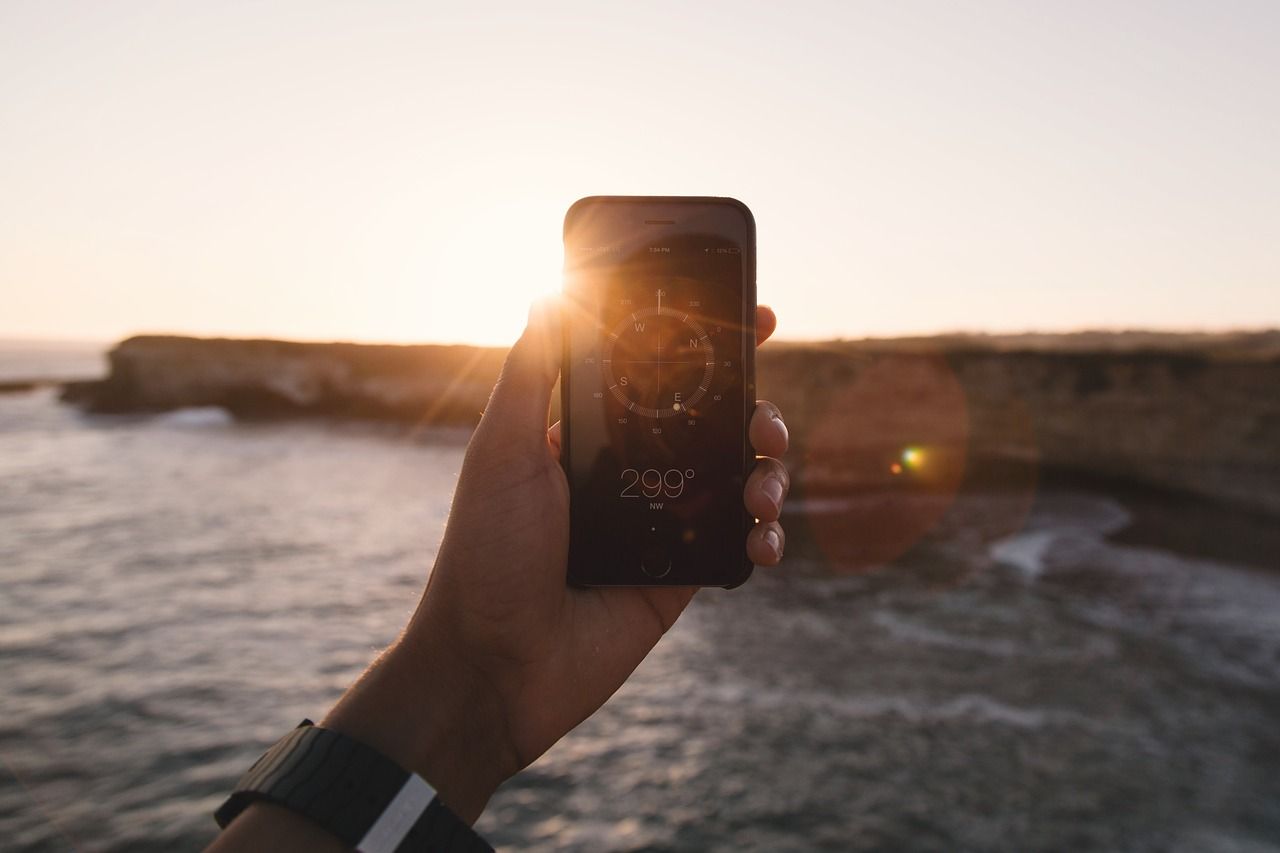 hand holding phone in front of ocean with compass app