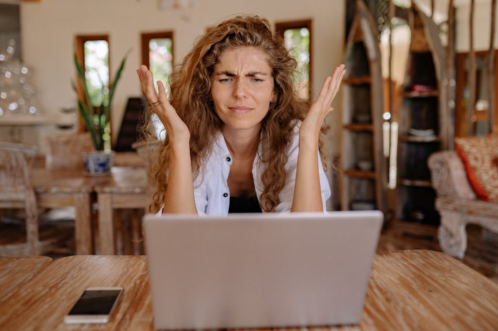 a woman lifting her hands up in frustration at her laptop