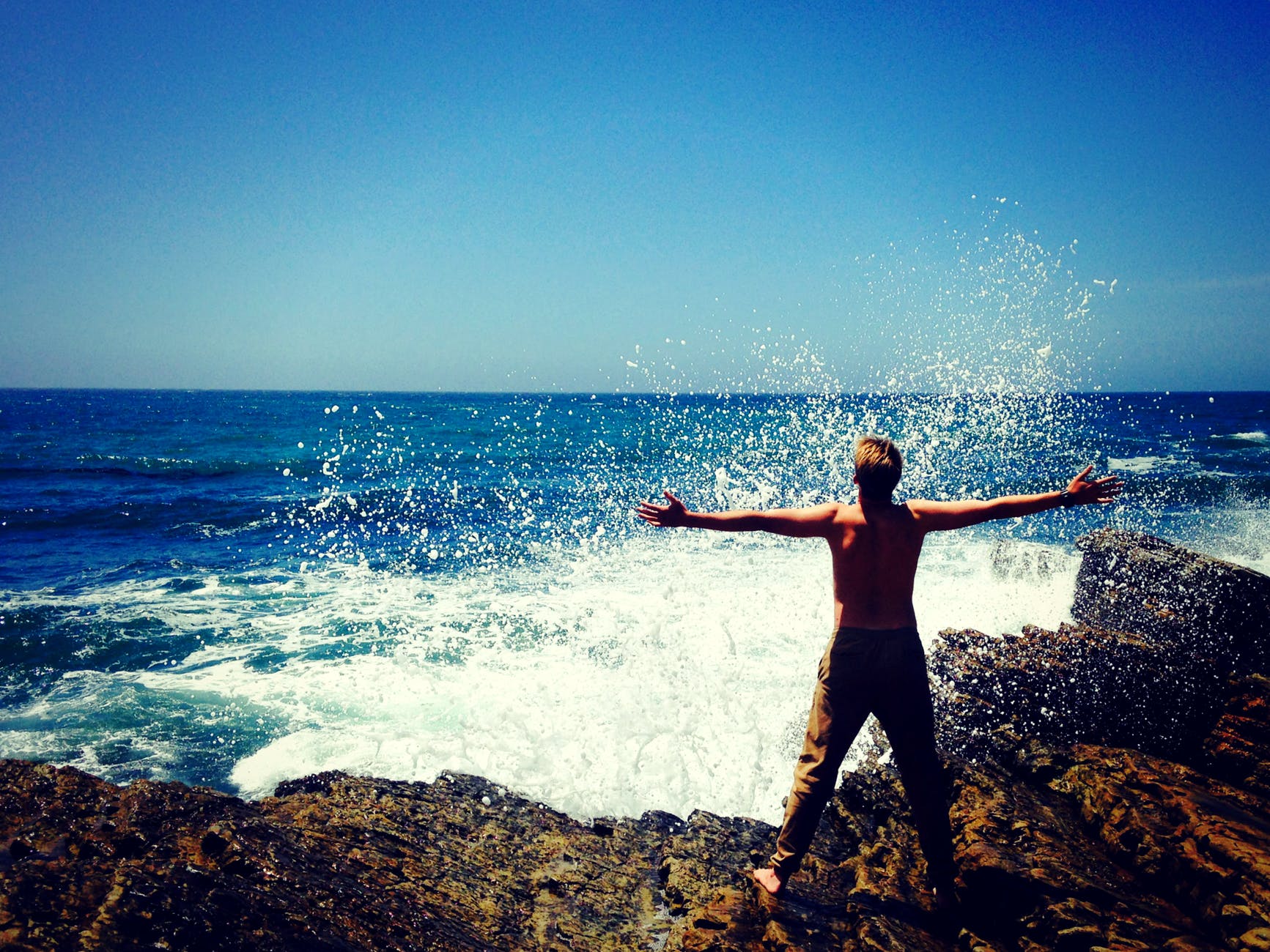 man holding arms wide in front of ocean