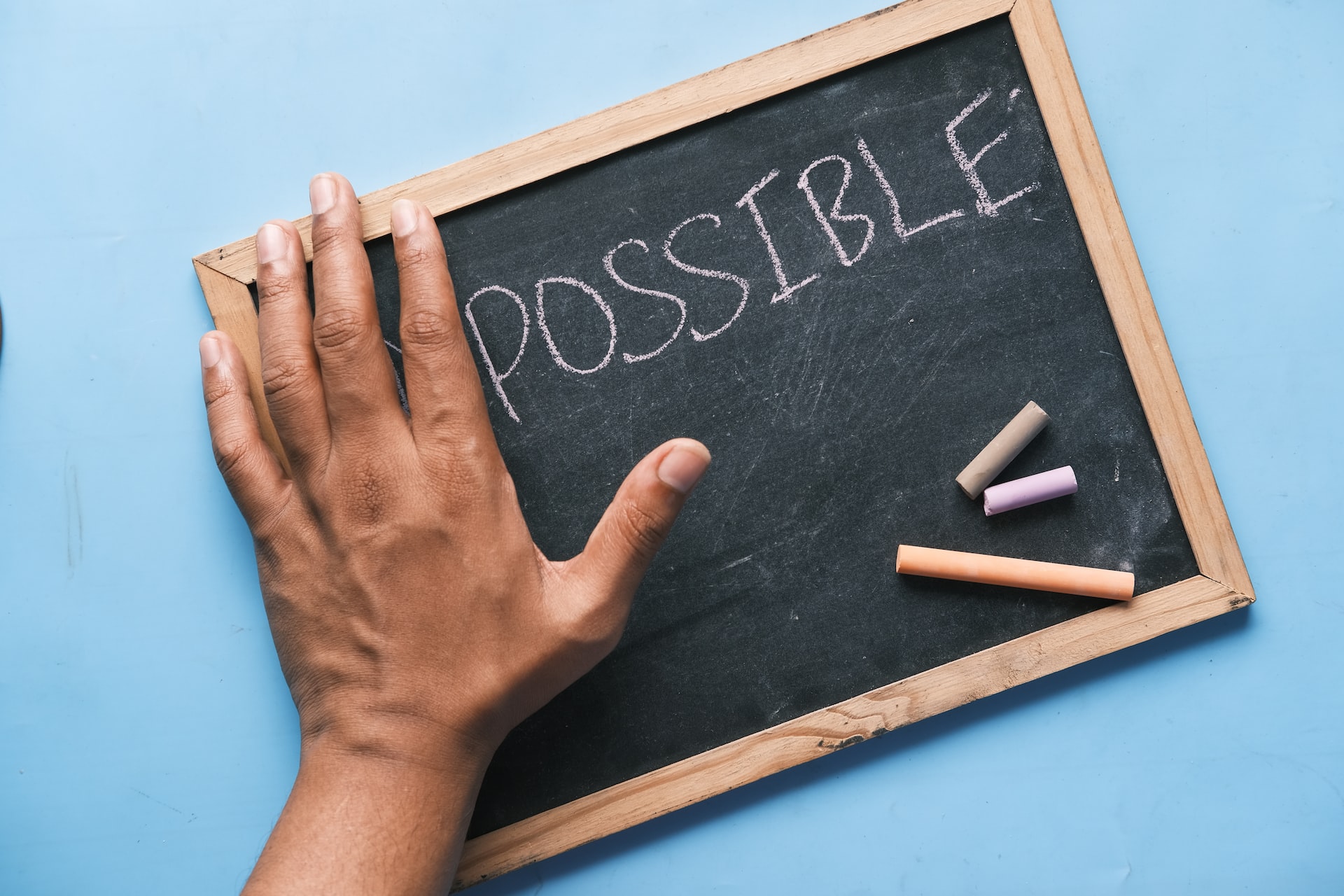 The word 'impossible' written on a chalkboard with a hand covering the 'im'