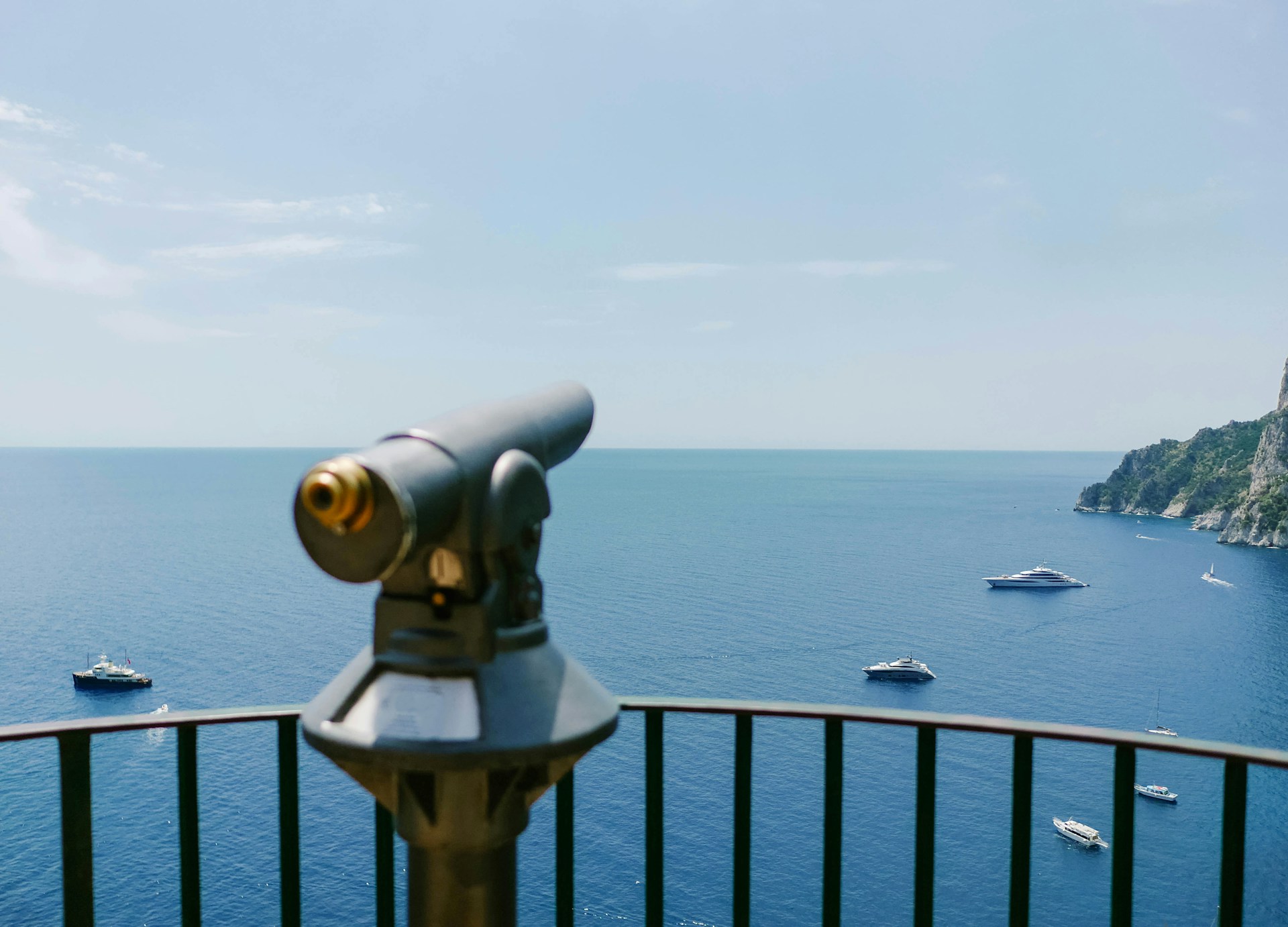 A telescope pointing at the ocean and various ships