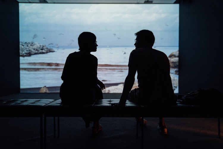 two people sitting in front of the ocean talking intently