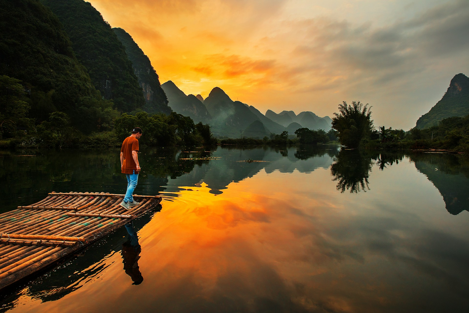 a man standing on a wooden raft on a tropical river at sunset