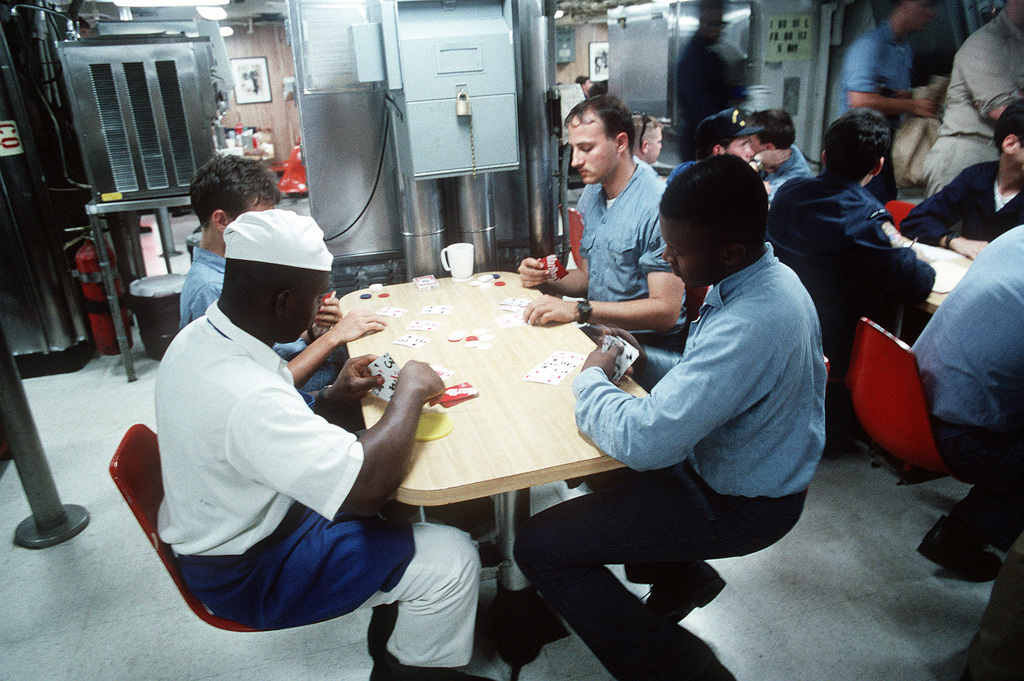 men working in various maritime jobs playing cards in the crew mess