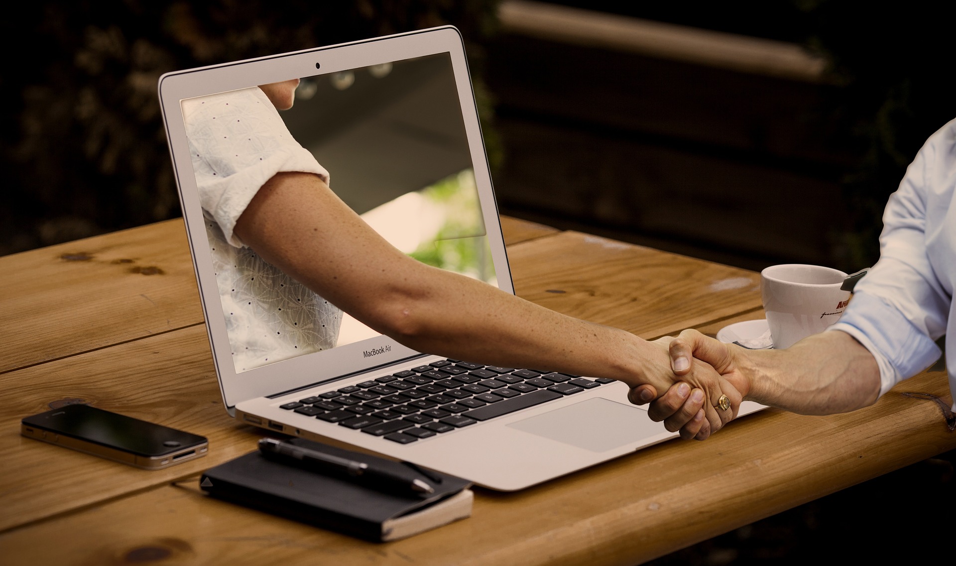 Two people shaking hands through a laptop screen