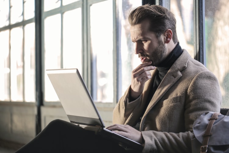 a man looking at his laptop while stroking his chin in thought