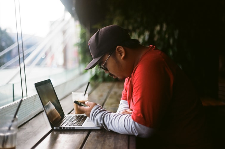 a man using his phone and a laptop in a cafe