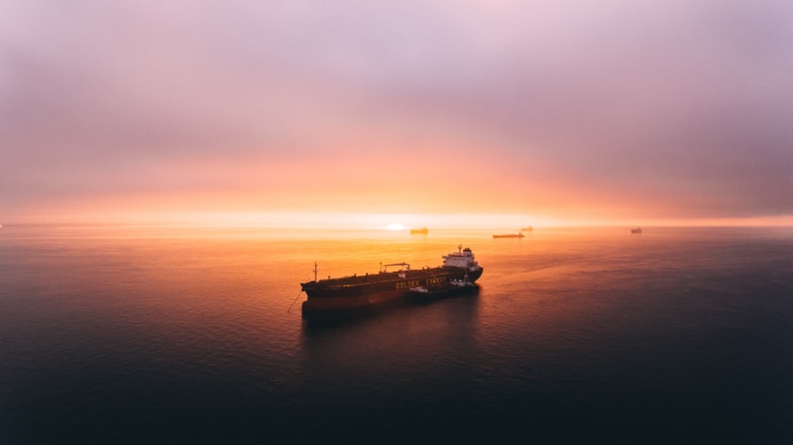 a cargo ship in the middle of the ocean at sunset