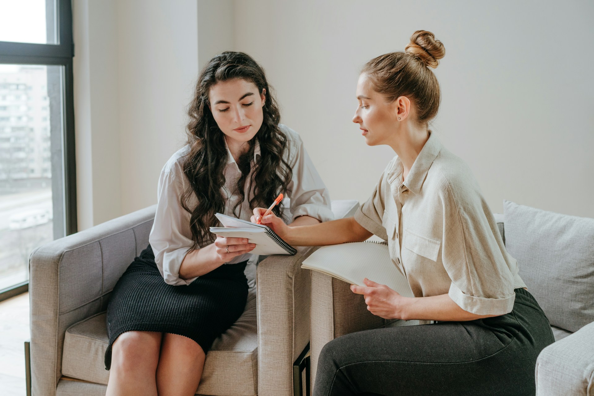 Two women in an office with one showing the other something in a notebook