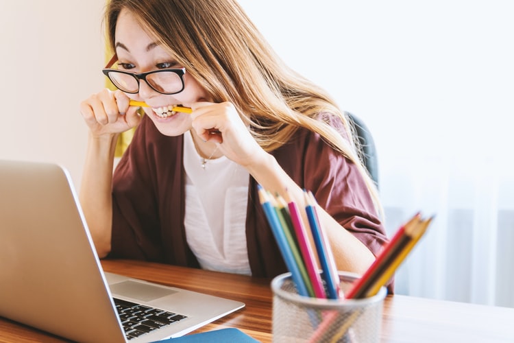 stressed woman looking at laptop while biting down on a pencil