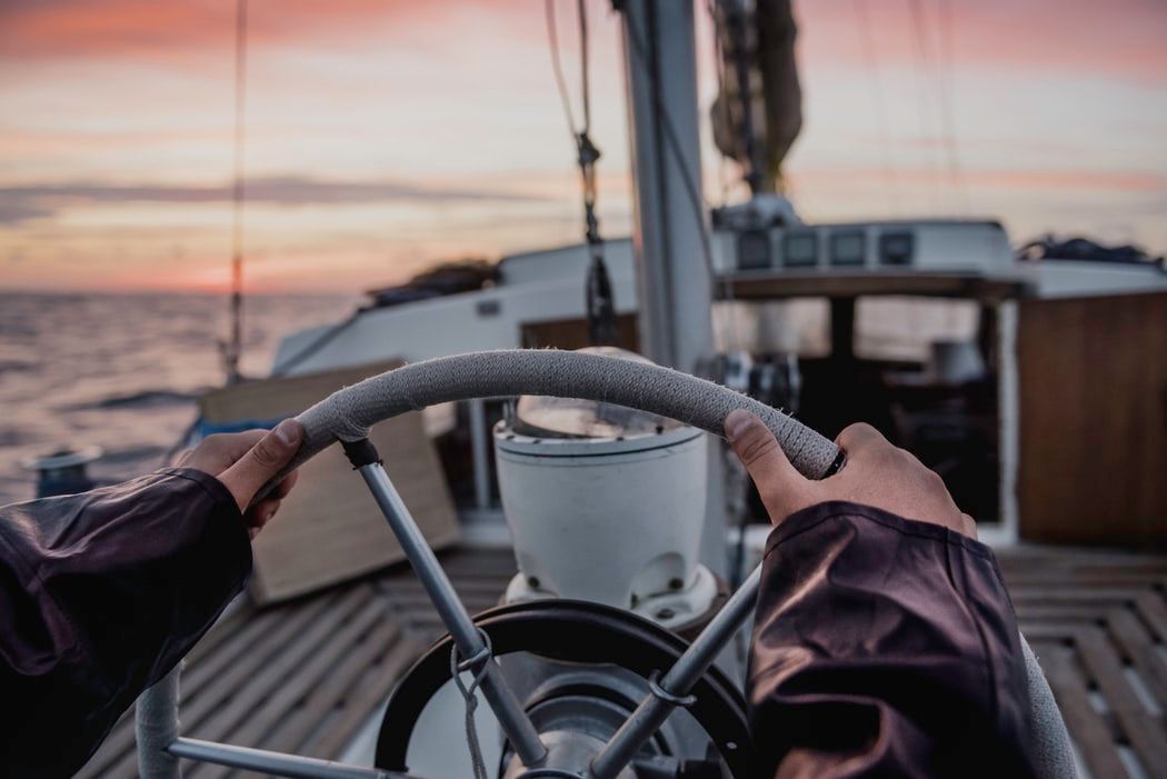 hands holding ship's wheel at sunset