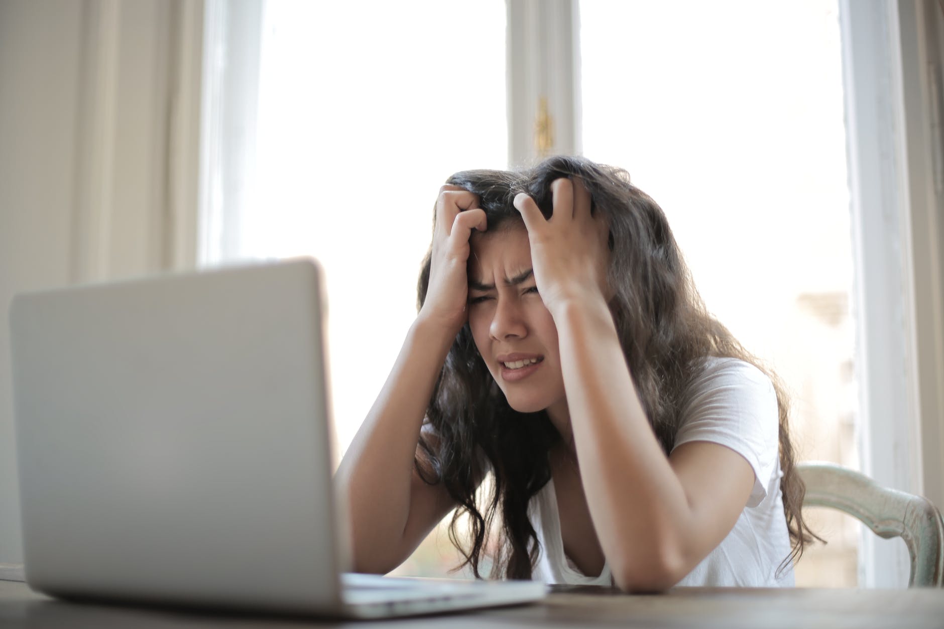 woman holding her head while looking at laptop