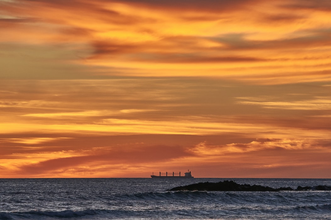 silhouette of a bulk carrier vessel on the horizon at sunset