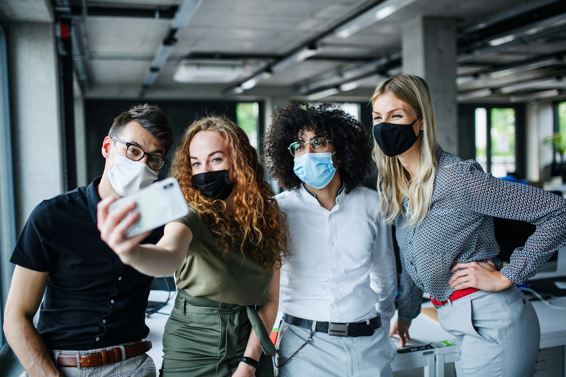 coworkers in an office taking a selfie while wearing facemasks