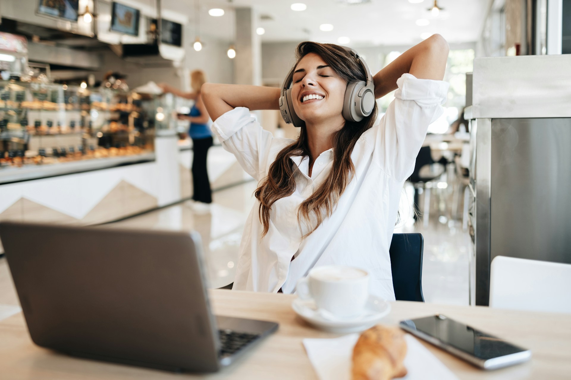 a woman in a coffee shop wearing Bluetooth headphones while using her laptop