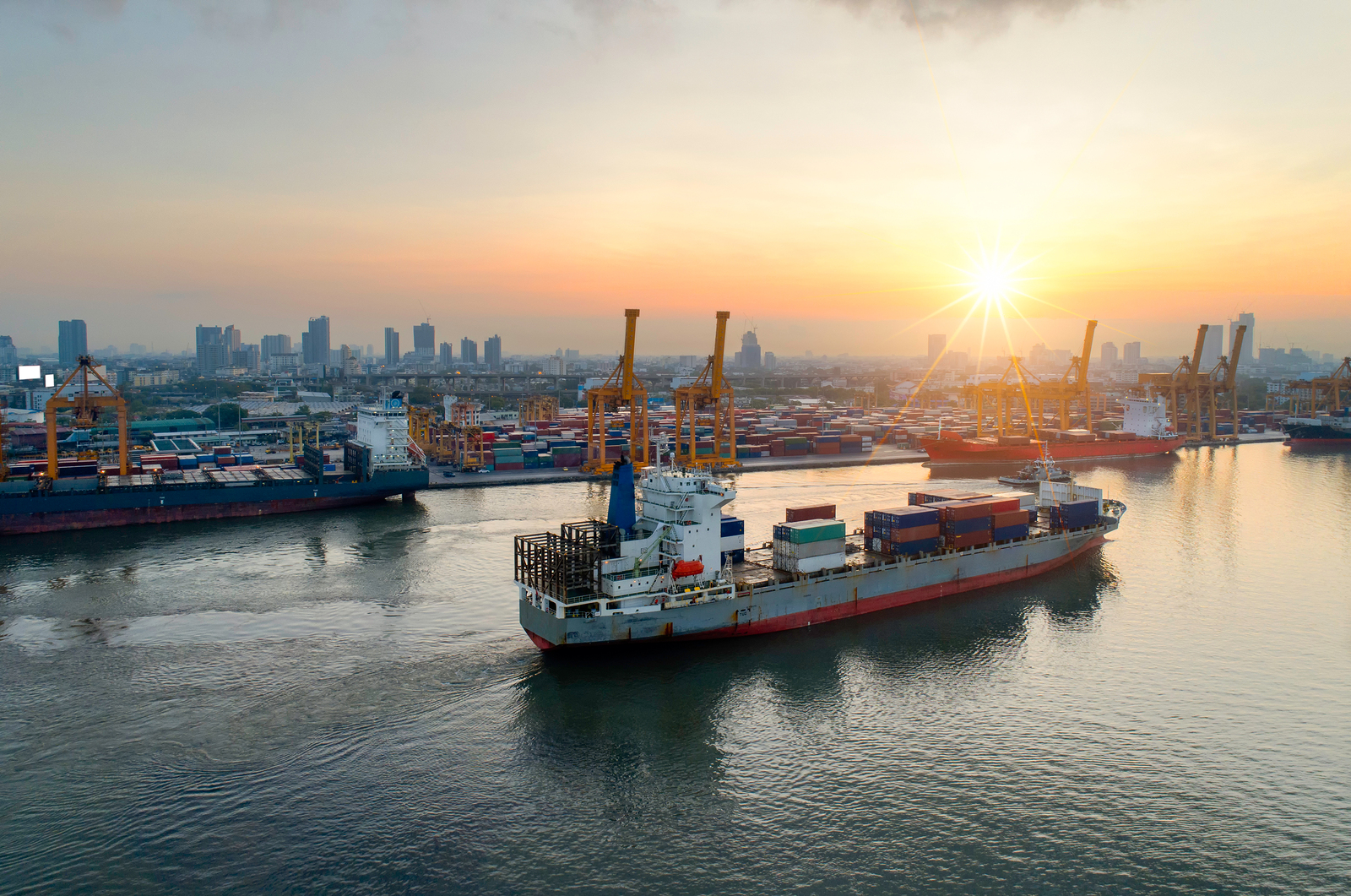 coaster vessel sailing past a port at sunset